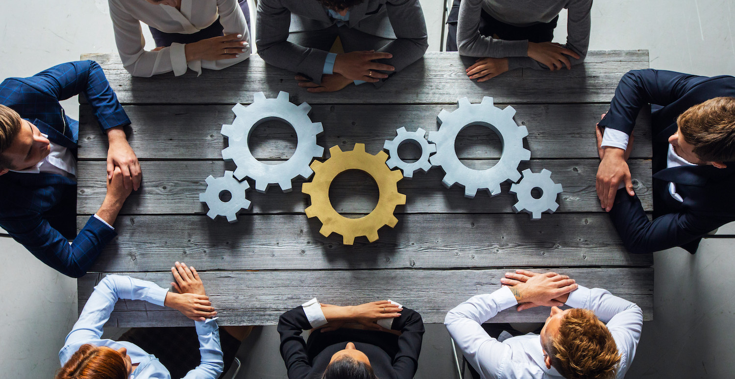 Group of business people joining together silver and golden colored gears on table at workplace top view